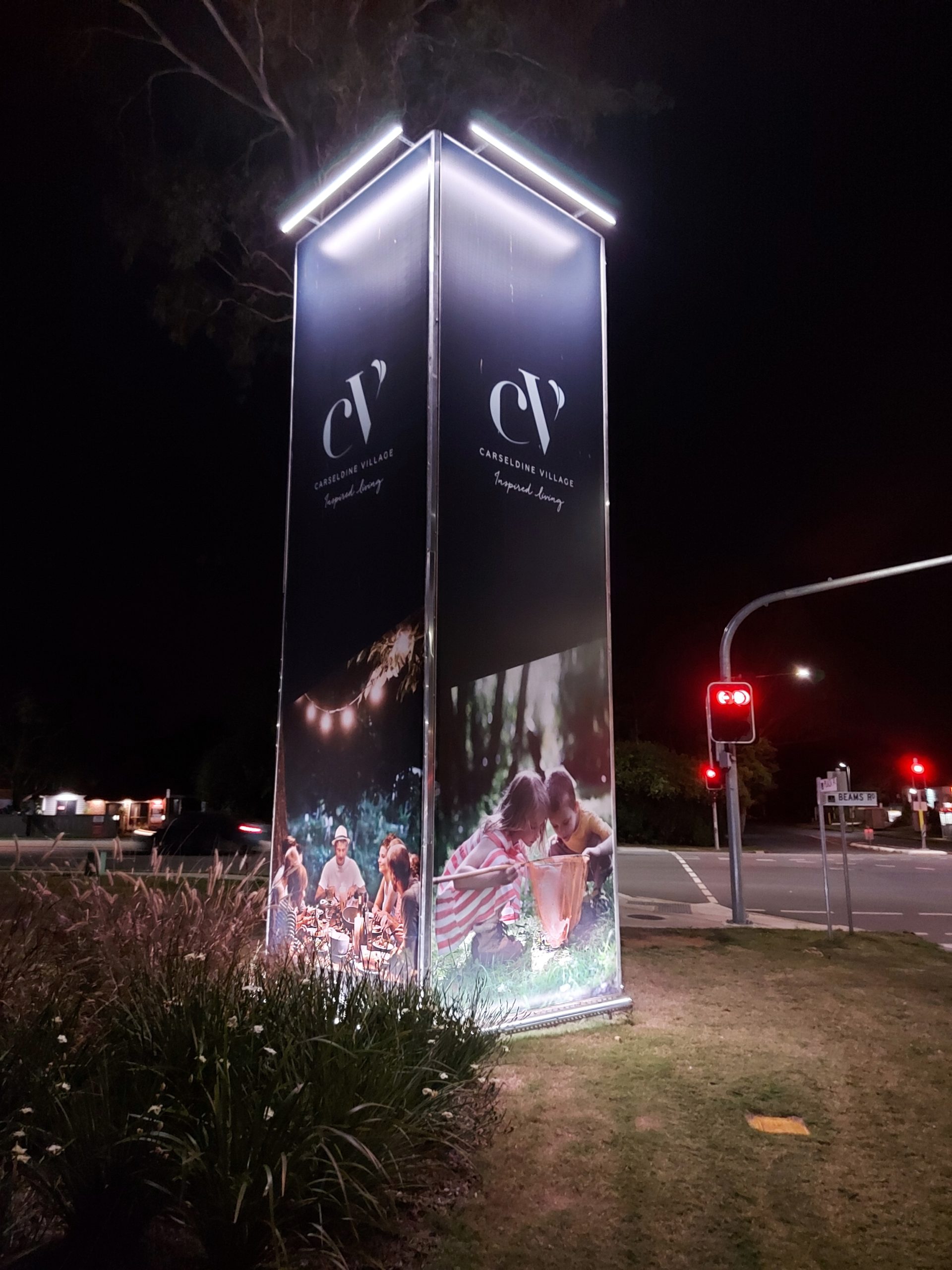 A large illuminated billboard project in the middle of a street.